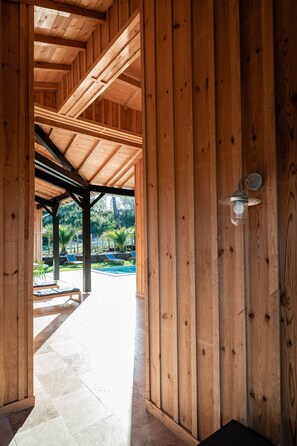 Una estructura de fusta amb terrassa coberta, seients a l'aire lliure i vista a una piscina.