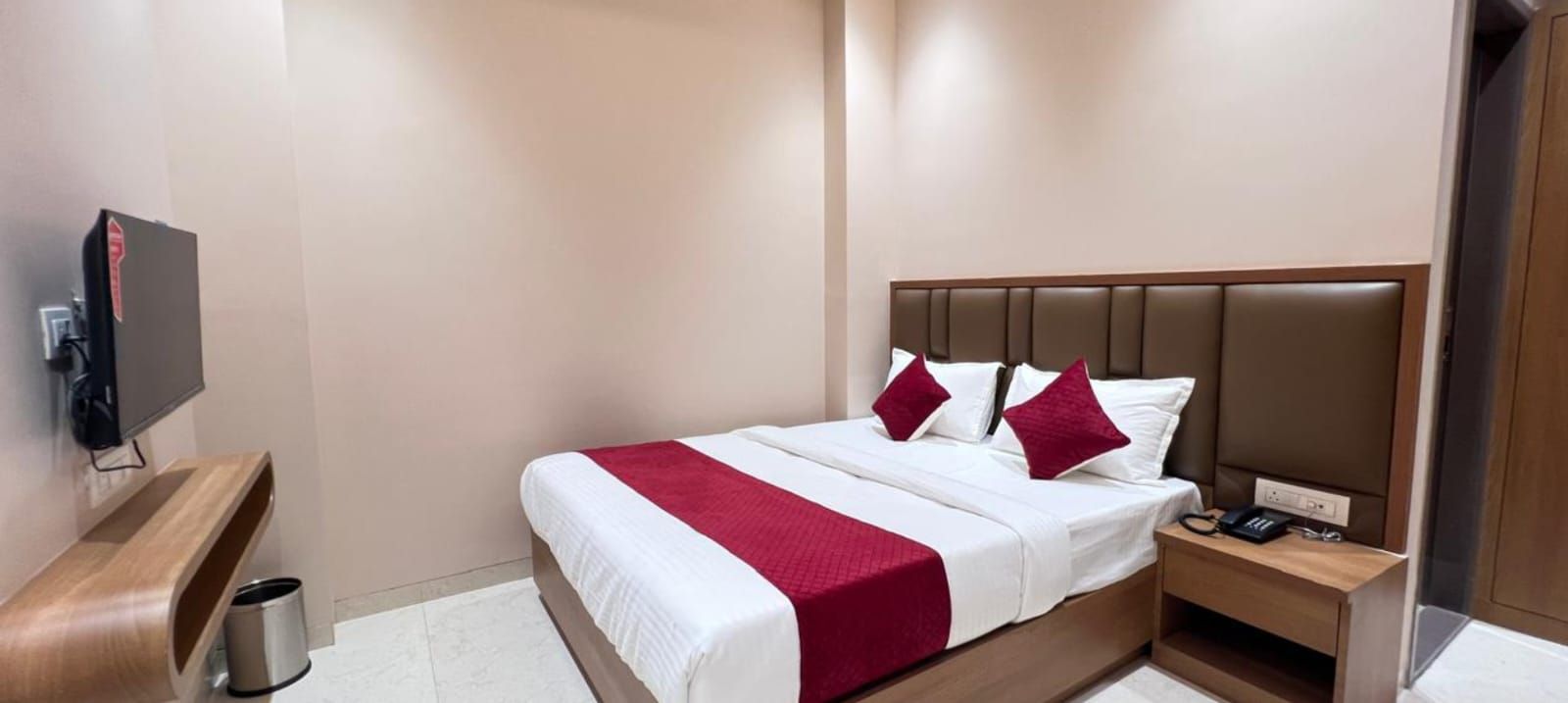 Una habitación de hotel con cama, mesita de noche, televisión y un cesto de basura.