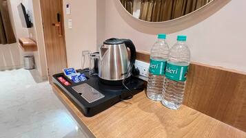 A hotel room with a wooden counter, a kettle, two water bottles, and a tray with a tea bag and glasses.