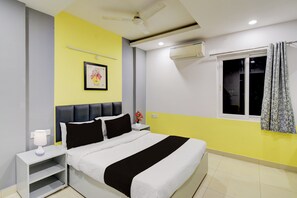 Un dormitorio con cama, mesitas de noche, ventilador de techo, aire acondicionado, ventana con cortinas e imagen colgada en la pared.