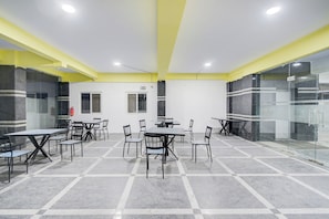 Un salón de conferencias con mesas y sillas, un extintor y una pared divisoria de vidrio.