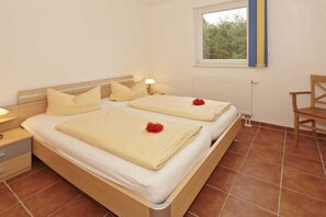 A double bed with a wooden frame, two bedside tables, a window with a view of greenery, and a radiator. - "Jonas" in the Riwa House (Kölpinsee)