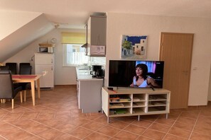 A living room with a television, a dining table with chairs, a kitchen area with a microwave, and a door. - "Jonas" in the Riwa House (Kölpinsee)