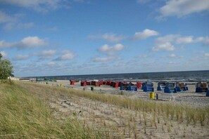 A beach with dunes, a row of beach huts, and the ocean in the background. - "Jonas" in the Riwa House (Kölpinsee)