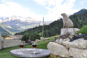 Ein Tisch mit zwei Weingläsern, einer Steinstatue und einer Berglandschaft im Hintergrund.