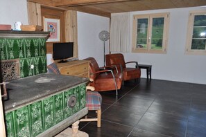 Habitació amb un armari verd, televisió, una cadira de pell marró i finestra amb vista a vegetació.