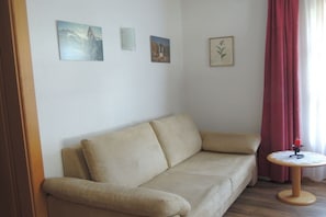 En beige soffa med ett litet runt bord och ett ljus, placerad framför en vit vägg med tre inramade tavlor.