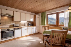 A kitchen with wooden cabinets, a built-in oven, and a dining area with a table and chairs. - Holiday apartment with 1 bedroom (Aschau)