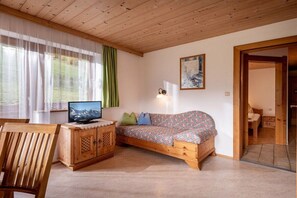 A cozy room with a wooden ceiling, a sofa with patterned cushions, a television on a wooden cabinet, and a painting on the wall. - Holiday apartment with 1 bedroom (Aschau)