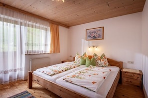 A bedroom with a wooden bed, a nightstand, a window with curtains, and a wall-mounted light fixture. - Holiday apartment with 1 bedroom (Aschau)