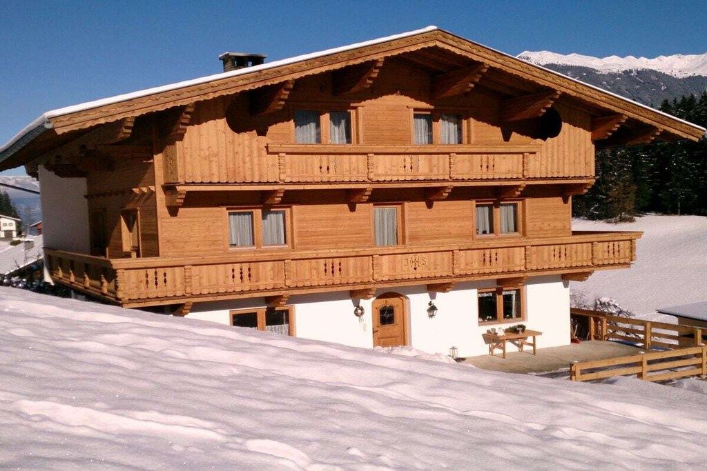 Eine Holzchalet mit Balkon, einer kleinen Veranda und Blick auf schneebedeckte Berge.