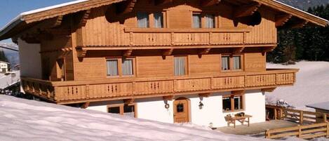 Eine Holzchalet mit Balkon, einer kleinen Veranda und Blick auf schneebedeckte Berge.