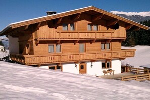 Eine Holzchalet mit Balkon, einer kleinen Veranda und Blick auf schneebedeckte Berge.