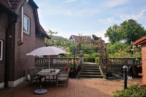 Een bakstenen huis met een patio, compleet met een tafel, stoelen, een witte parasol en een trap naar een tuin.