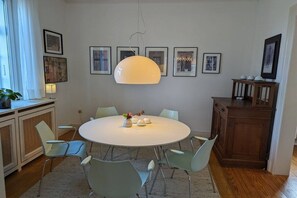 Ein Essbereich mit einem runden Tisch, sechs Stühlen, einer Hängelampe und gerahmten Bildern an der Wand.
