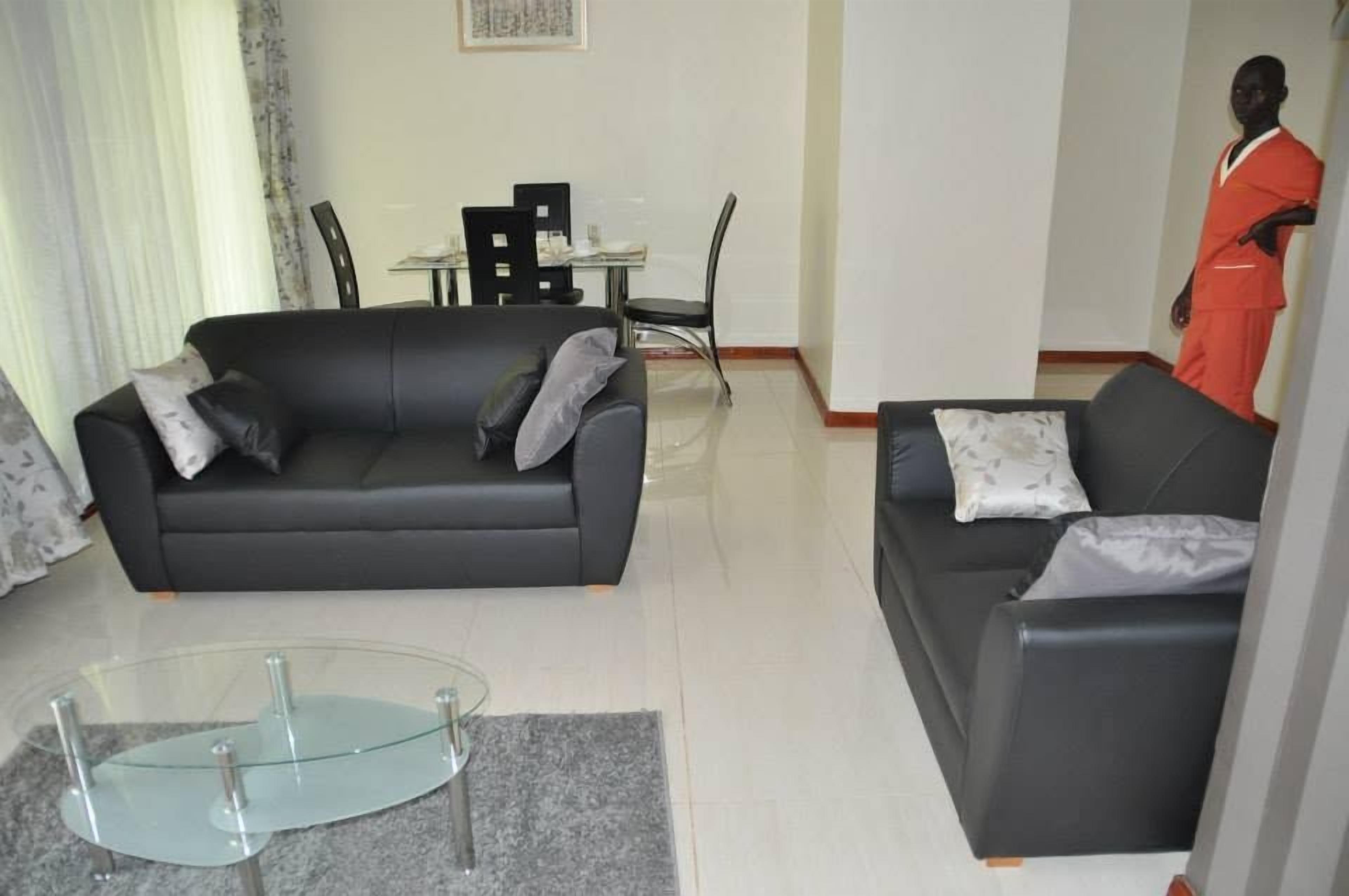 A living room with a black sofa, a glass coffee table, and a dining area with chairs and a table.