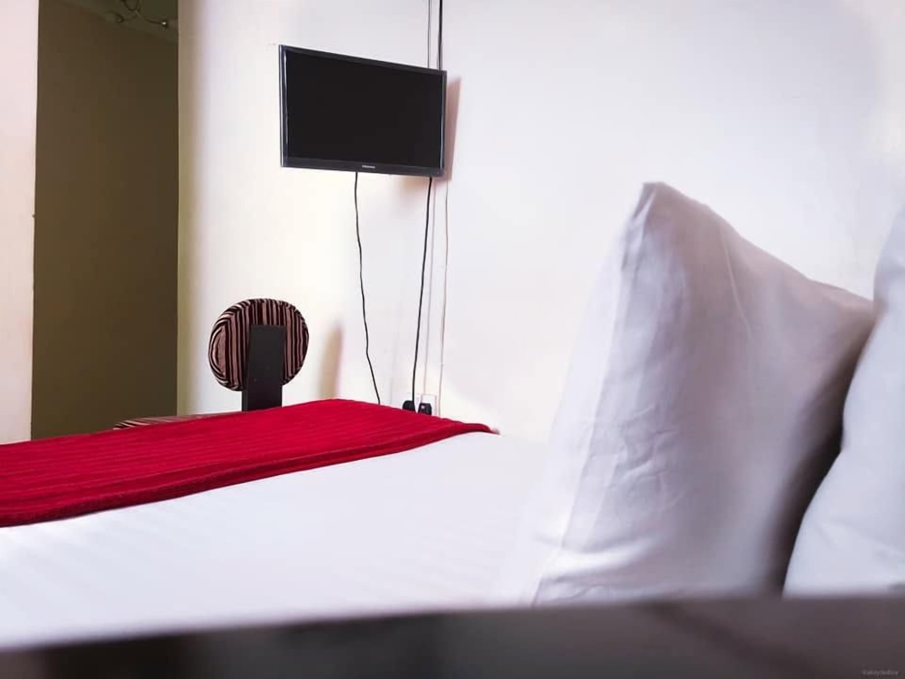 A hotel room with a bed, a flat-screen TV mounted on the wall, and a red throw blanket.