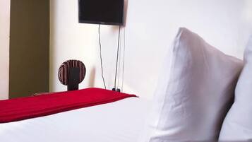 A hotel room with a bed, a flat-screen TV mounted on the wall, and a red throw blanket.
