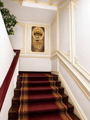 Una majestuosa escalera con alfombra roja y detalles dorados, que conduce a una habitación con un panel decorativo en la pared.