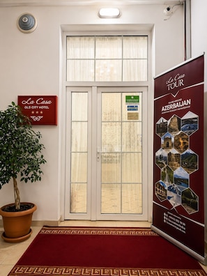 A hotel entrance with a double door, a signboard for La Casa Old City Hotel, a promotional poster for tours around Azerbaijan, and a potted plant. - La Casa Nizami Street (Baku)