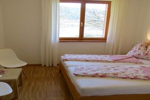A room with two beds, a chair, a table, and a window with curtains. - Holiday apartment with 1 bedroom (Steindorf)