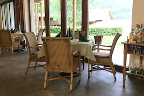 A dining area with wicker chairs, a table with a white tablecloth, and a view of greenery outside. - Holiday apartment with 1 bedroom (Steindorf)
