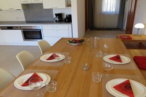 A dining area with a wooden table set for four, white chairs, and a kitchen in the background. - Holiday apartment with 1 bedroom (Steindorf)