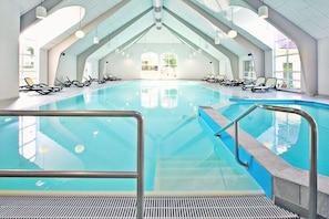 Ein heller, überdachter Innenpool mit klarem Wasser, umgeben von Liegestühlen.