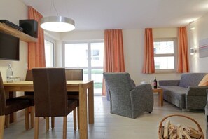 Ein Wohnzimmer mit Esstisch, Stühlen, einer Couch und einem an der Wand montierten Fernseher.