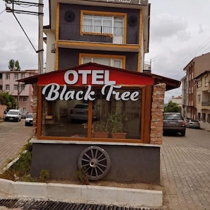 Un hotel llamado 'OTEL Black Tree' con un toldo rojo distintivo y un amplio ventanal.