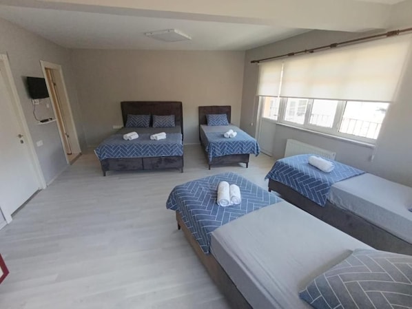 A hotel room with three beds, a television, and a window with blinds.