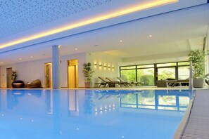 Ein moderner Innenpool mit klarem Wasser, Liegestühlen und Pflanzen in Töpfen.