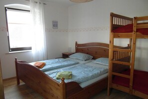 Een kamer met een houten bed, een stapelbed, een raam met gordijnen en een klein nachtkastje.