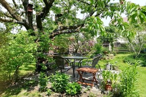 An outdoor patio with a table and chairs, surrounded by greenery and a tree. - Holiday apartment with 1 bedroom (Rathewalde)