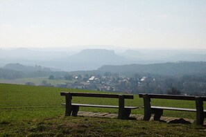 A bench in a grassy field with a view of a village and distant hills. - Holiday apartment with 1 bedroom (Rathewalde)