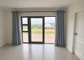 Ein Zimmer mit einer großen Schiebeglastür, die zu einem Außenbereich führt, sowie einer weißen Tür rechts und einem gefliesten Boden.