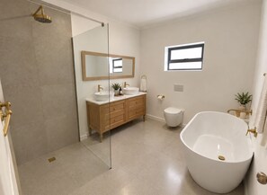 Ein modernes Badezimmer mit einer freistehenden Badewanne, einer Duschkabine aus Glas, einem Waschtisch mit zwei Becken und einer Toilette.