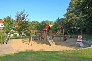 Une aire de jeux avec une structure d’escalade en bois, un toboggan et une maisonnette avec un toit rouge.