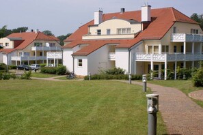 Eine Reihe von zweigeschossigen Häusern mit roten Ziegeldächern, einem gepflasterten Weg und einer Rasenfläche.