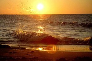 Un coucher de soleil sur l’océan, avec des vagues qui déferlent sur le rivage.