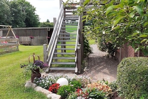 A wooden staircase leading to a covered area, surrounded by a garden with various plants and flowers. - Holiday apartment with 2 bedrooms (Sehestedt)