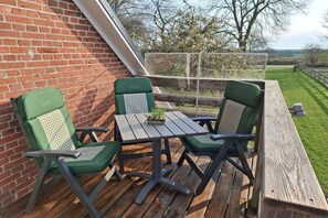 A wooden deck with a table and two chairs, a brick wall, and a view of the countryside. - Holiday apartment with 2 bedrooms (Sehestedt)