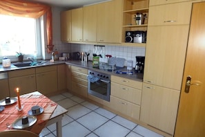 A kitchen with wooden cabinets, a stove, and a window with curtains. - Holiday home with 3 bedrooms (Drochtersen)