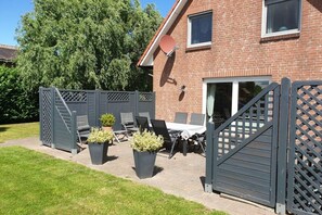 A brick house with a patio area featuring a table and chairs, a satellite dish, and a gated entrance. - Holiday home with 3 bedrooms (Drochtersen)