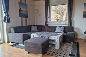 A modern living room with a grey sofa, a coffee table, and an ottoman. - Holiday home with 3 bedrooms (Drochtersen)
