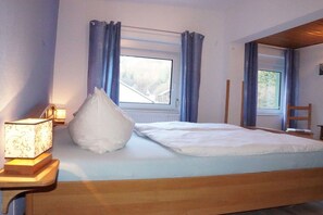 A bedroom with a bed, a bedside table with a lamp, a window with curtains, and a view of the outside. - Holiday apartment with 2 bedrooms (Bad Schandau Stadtteil Prossen)