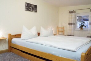A single bed with a wooden frame, white bedding, a small bedside table, a chair, a radiator, a window with curtains, and a wall-mounted picture. - Holiday apartment with 2 bedrooms (Bad Schandau Stadtteil Prossen)