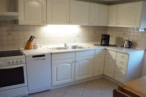 A kitchen with white cabinets, a stove, a sink, and a coffee maker. - Holiday apartment with 2 bedrooms (Bad Schandau Stadtteil Prossen)