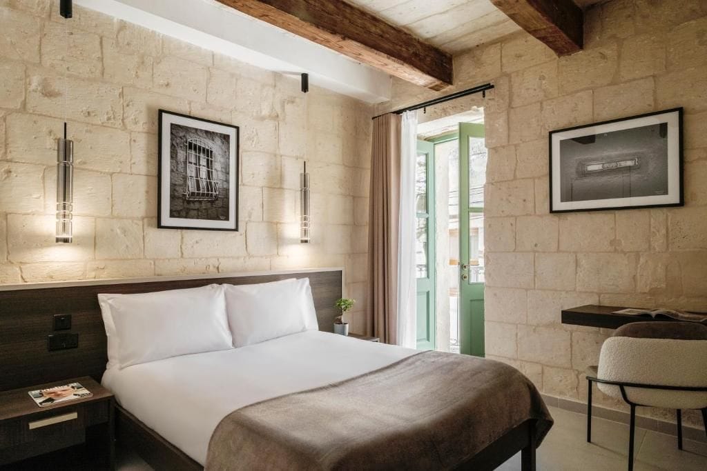 Una habitación de hotel con cama, mesita de noche, lámpara, cuadros enmarcados y una silla.