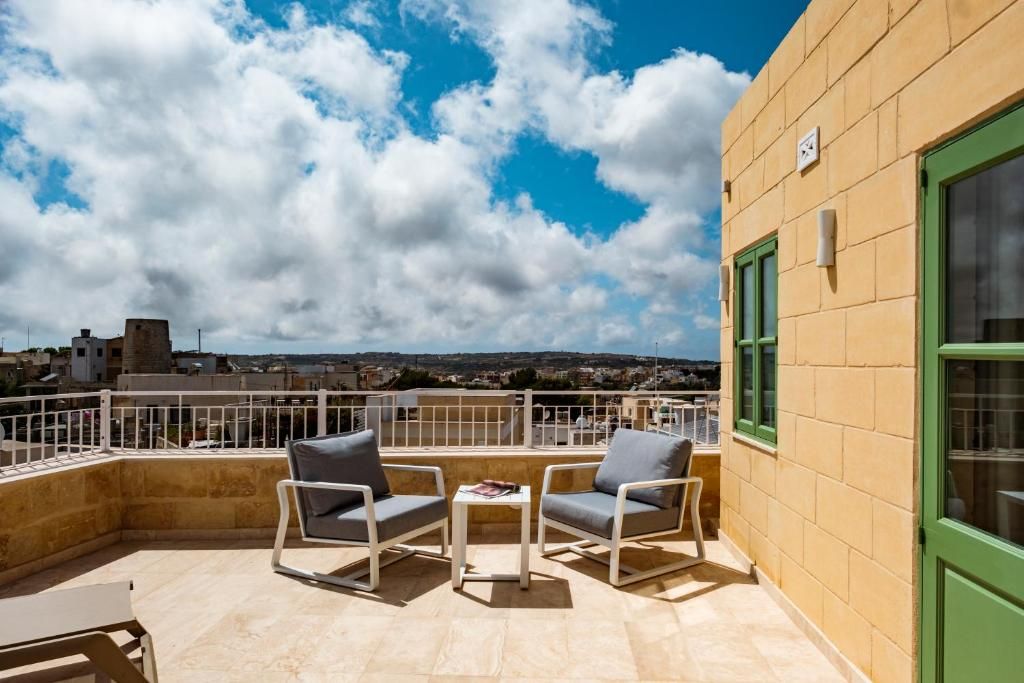 A terrace with two chairs and a table, a green window, and a view of buildings and hills.